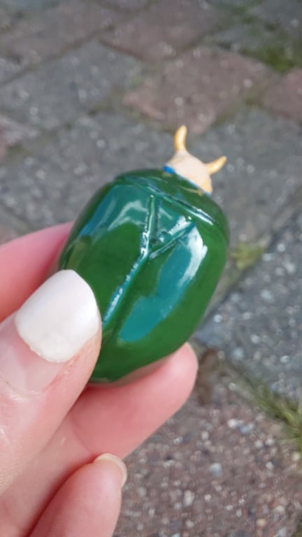 Hånd, der holder en grøn, blankt malet figur formet som en lille okse med gule horn.