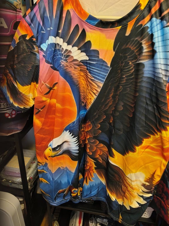 Farverig T-shirt med stort tryk af en ørn i flugt mod en orange og blå baggrund.