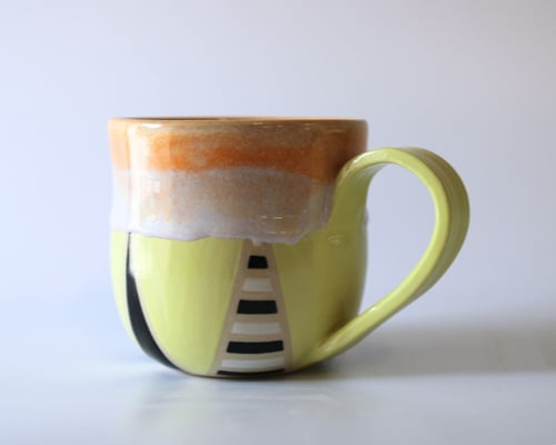 Keramisk kaffekop med gul skygge, orange og hvid glasur øverst, og sort-hvidt stribet motiv på siden. (1)