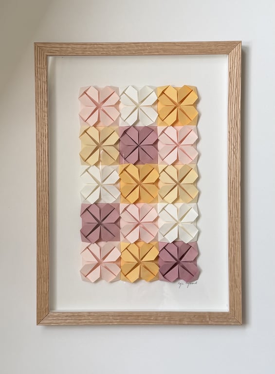 Billedramme med 16 foldede papirblomster i pastel farver arrangeret i et 4x4 grid.