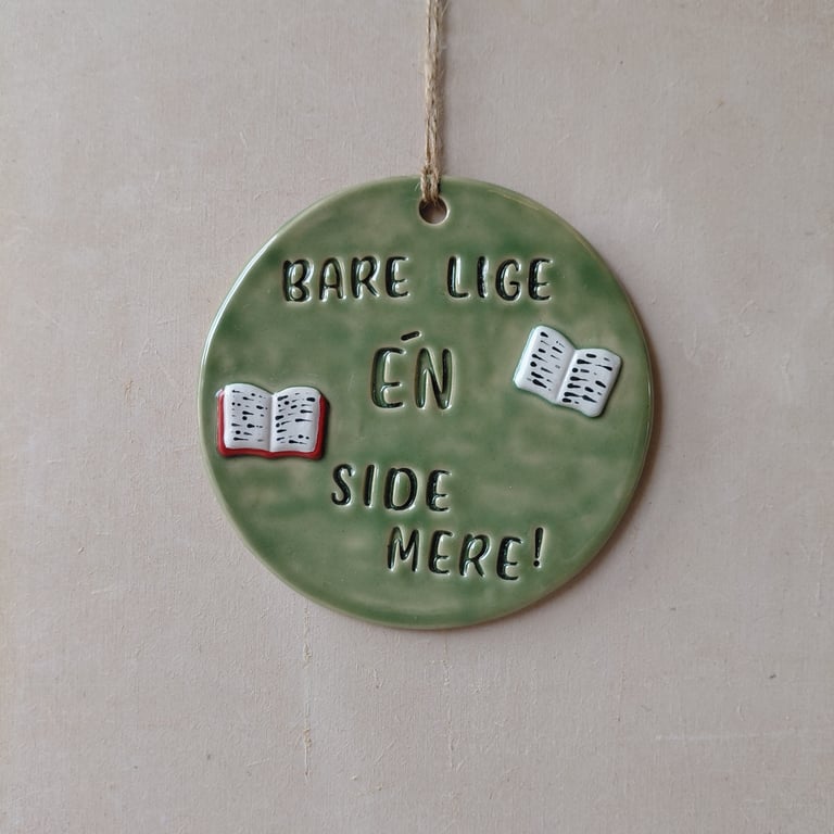 Grøn rund keramisk ophæng med teksten "Bare lige én side mere!" samt to små illustrerede åbne bøger.
