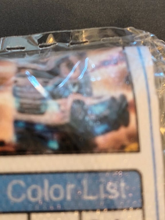 Nærbillede af en plastindpakket genstand med et sløret billede af en bil og teksten "Color List".