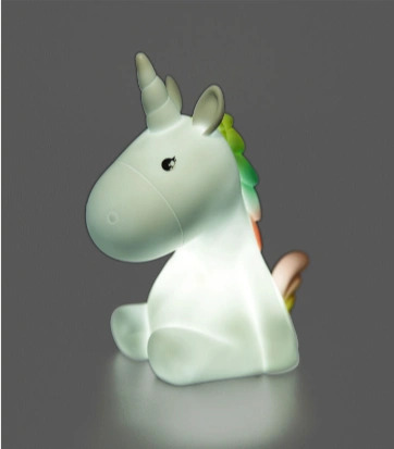 En lille lampe formet som en hvid enhjørning med regnbuefarvet manke og et blødt lys, der lyser op mod en grå baggrund.