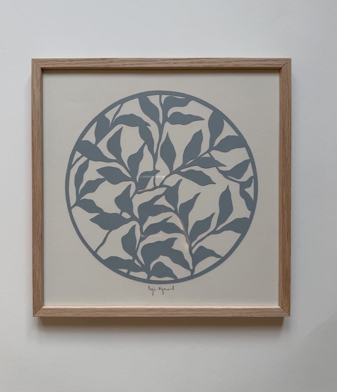 Billede af en indrammet kunstplakat med grågrønne blade i en cirkel på beige baggrund.