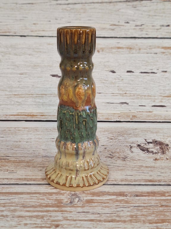 Keramisk lysestage med flerfarvet glasur i nuancer af brun, grøn og beige, placeret på træbord.
