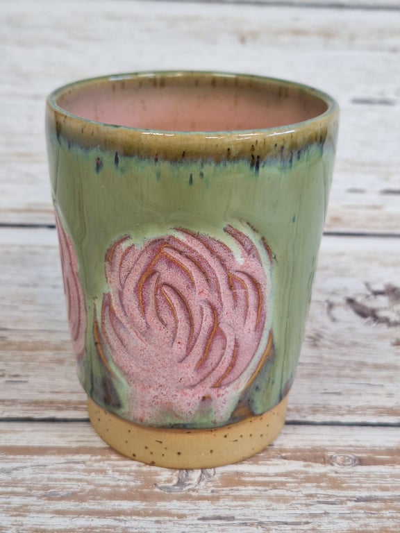 Keramisk kop med grøn glasur og pink blomstermønster, stående på lyst træbord.