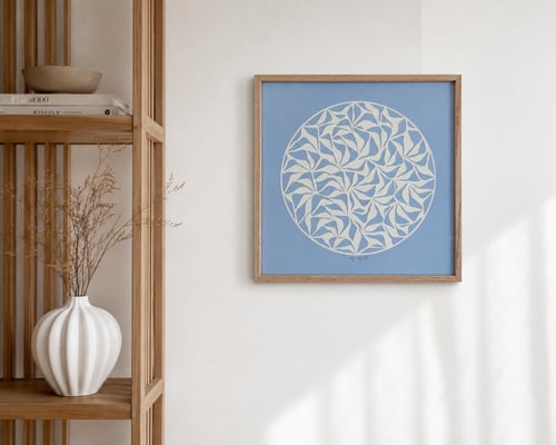 Billedvæg med en blå, firkantet plakat med hvidt cirkelmønster, ved siden af et lyst træreol med en hvid keramikvase med tørrede blomster. (1)