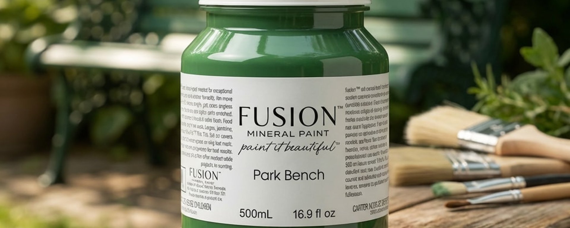 En flaske Fusion mineralmaling i farven Cast Iron omgivet af en antik globus, åbne bøger, håndskrevne breve, en lommeur, en lille guld styrerem og en sort notesbog med en fjerpen på en sort baggrund.