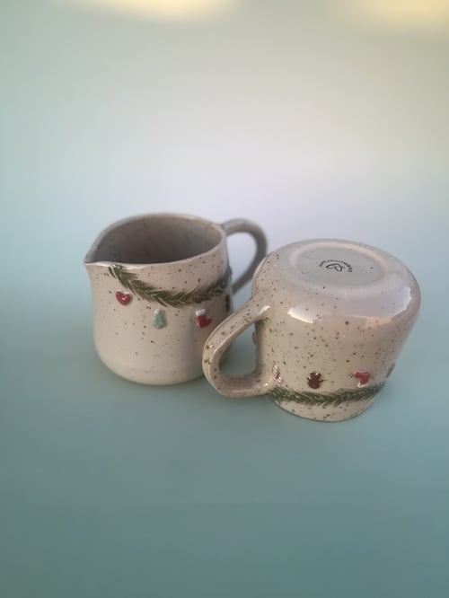 To kopper i beige keramik med grønne, røde og blå julepyntdetaljer, på lyseblå baggrund. (1)