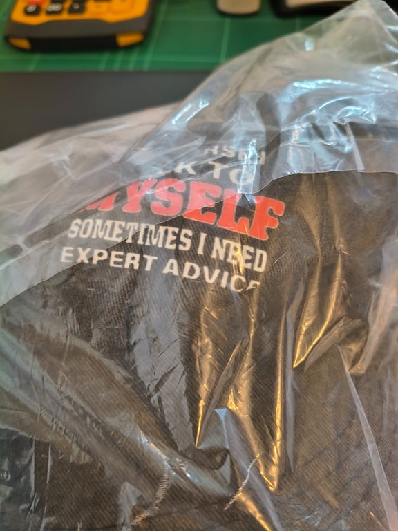 Sort t-shirt med teksten "ASK TO MYSELF SOMETIMES I NEED EXPERT ADVICE" pakket ind i en klar plastikpose.