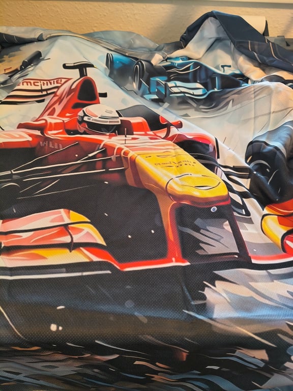 Billede af et lagnet med tryk af en Formel 1-racerkører i rød og gul køreposition.