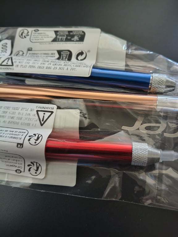 To metalværktøjer i farverne blå, kobber og rød pakket enkeltvis i gennemsigtige plastikposer med advarselsmærkater.
