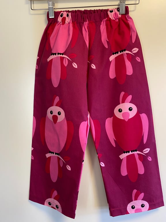 Bukser til børn med elastisk linning, mørkerød og pink med mønster af stiliserede papegøjer.