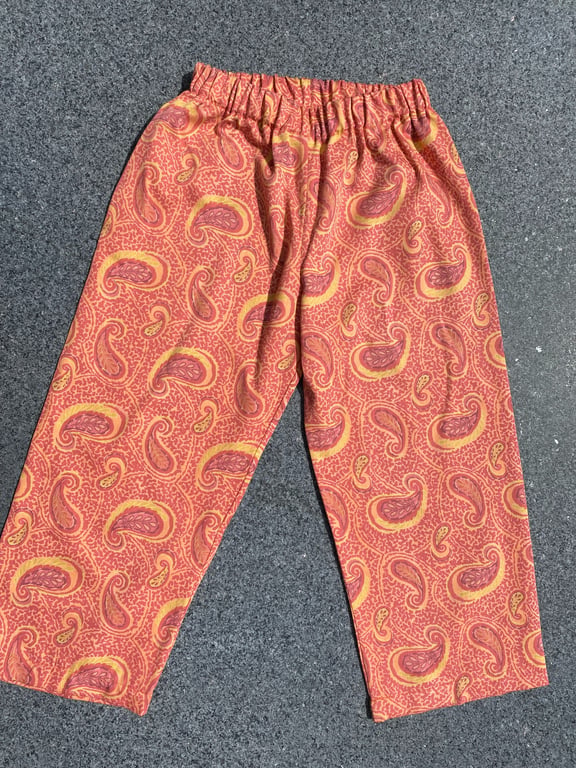 Bukser med elastisk talje og orange mønster med paisley-motiver, lagt fladt på grå baggrund.