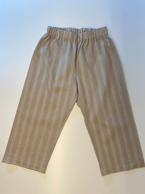 Børnebukser med elastisk talje og vertikale striber i beige og hvid.