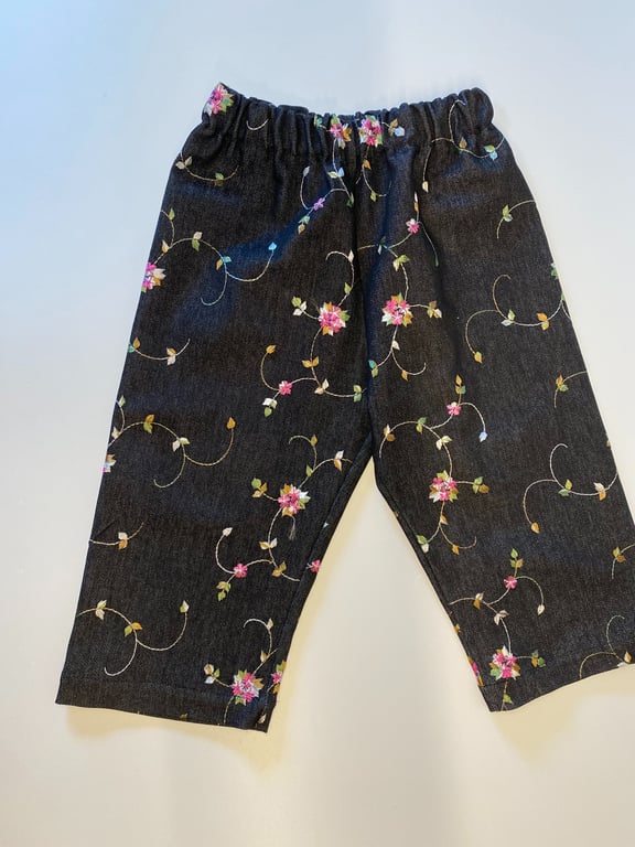 Sort bukser med elastisk talje og blomsterprint i pink, grøn og lyse farver på hvid baggrund.