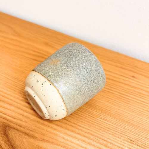Keramisk kop med grå og beige glasur liggende på et lysttræsbord. (1)