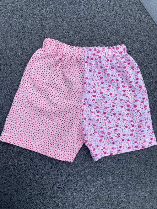 Pink børneshorts med elastisk talje og to forskellige mønstre; venstre side med små røde stjerner og højre side med små blomster. (1)