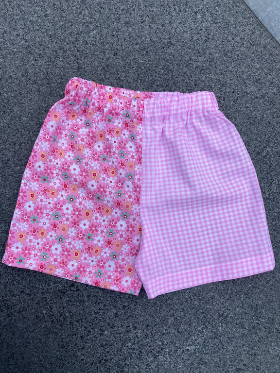 Lyserøde shorts med elastik i taljen, delt i to mønstre: blomsterprint på venstre side og lyserødt ginghamternet mønster på højre side.