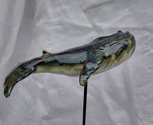 Keramisk figur af en hval med en blank, grønlig blå glasur, monteret på en sort metalstang mod en hvid baggrund. (1)
