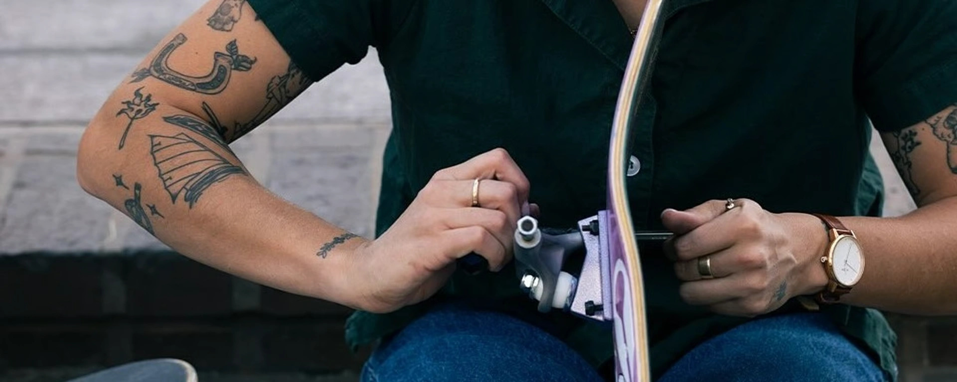 Person med tatoverede arme strammer skruer på et skateboard.
