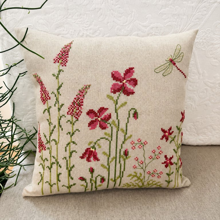 Pudebetræk med korsstingsbroderi af røde blomster og en guldsmed på beige stof.