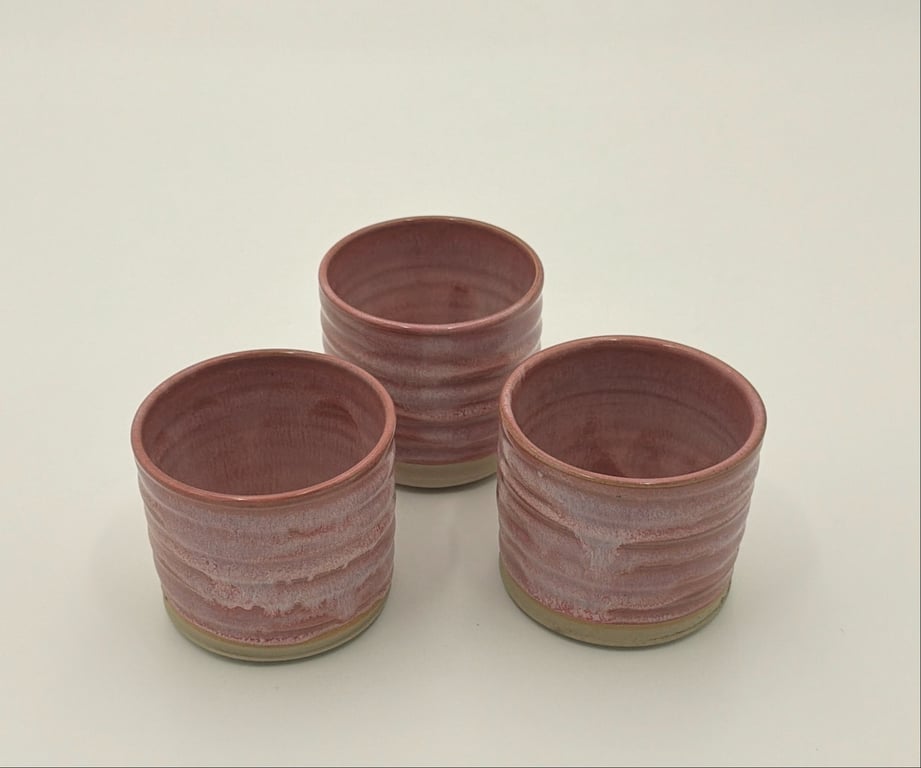 Tre små, runde keramikkrus med en pink og beige glasur på en hvid overflade.