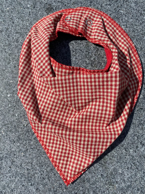 Rødt og hvidt ternet baby-bib eller halstørklæde med trykknapper på grå overflade.