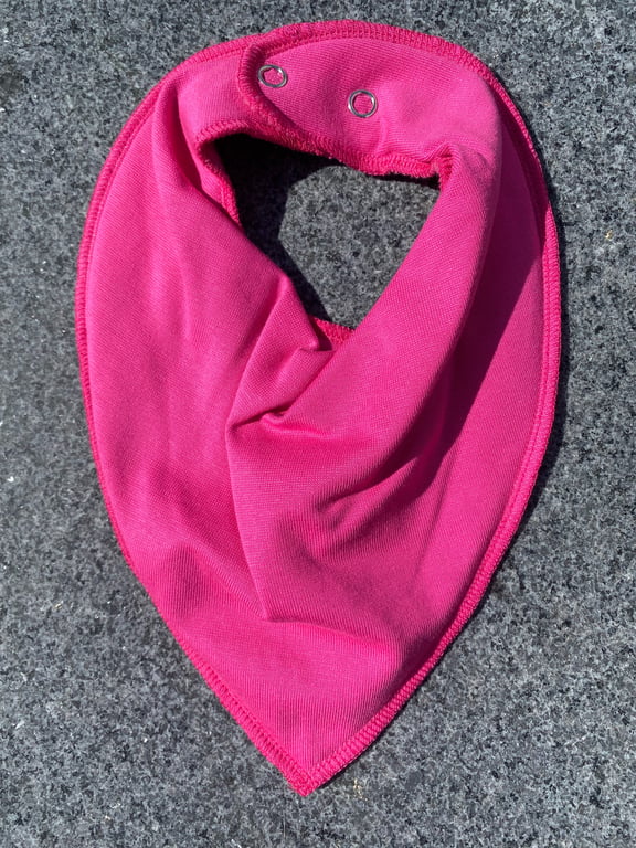 Pink trekantet stofble med trykknapper lagt på mørk grå overflade.
