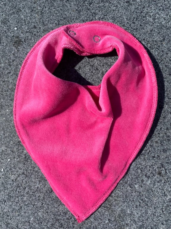 Pink stofhagesmæk med tryklåse, lagt på grå asfalt.
