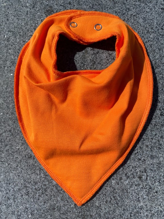 Orange trekantet baby- eller børnesmæk med trykknapper, lagt fladt på grå stenoverflade.