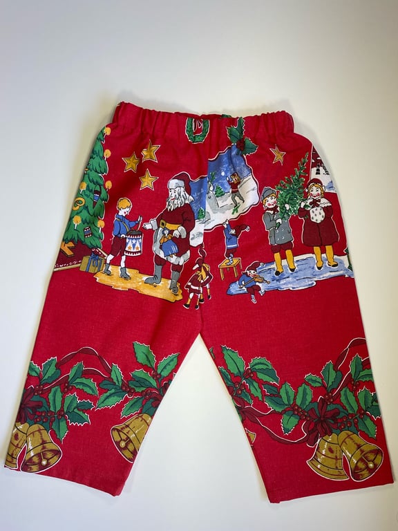 Kort juleshorts til børn med rød baggrund og julemotiver såsom nisser, klokker, kristtjørn og julestjerner.