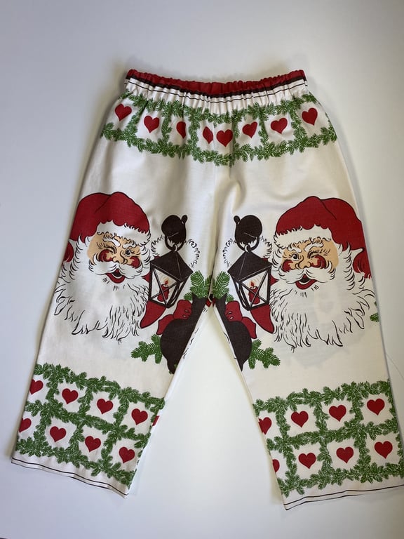 Billede af hvide bukser med julemotiver, herunder store billeder af julemandens ansigt, grønne grankranse og røde hjerter.