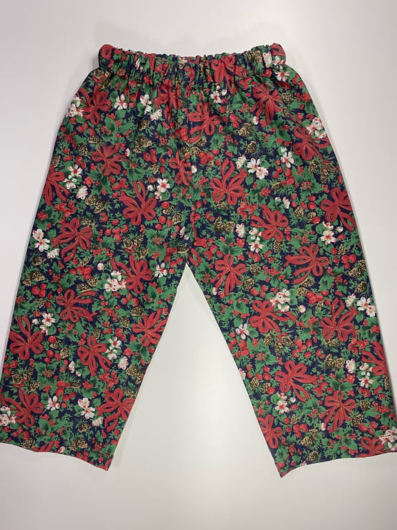 Bukser med elastik i taljen og blomsterprint i grøn, rød, hvid og blå farver, lagt fladt på en lys baggrund.