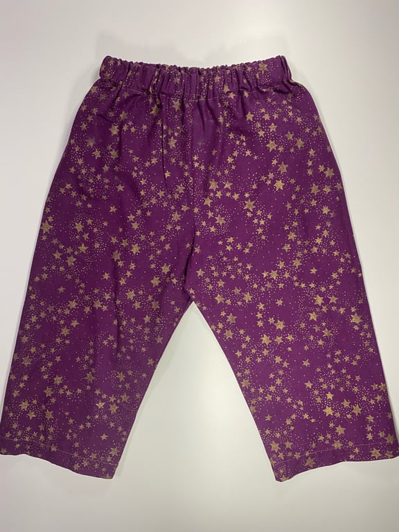 Lilla bukser med elastisk talje og guldfarvede stjerner spredt over stoffet.