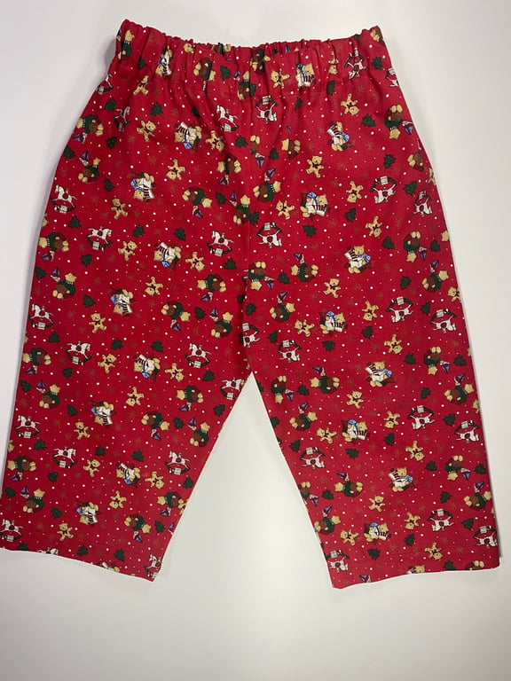 Børnepyjamasbukser i rød med julemotiv, herunder små nisser, juletræer og honningkager.