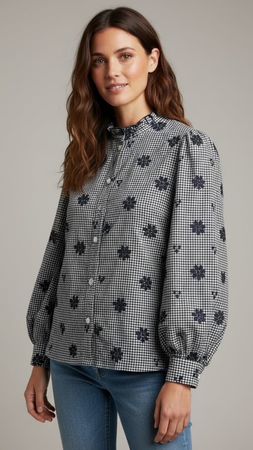 Kvinde iført sort-og-hvid ternet skjorte med mørke blomster, puffede ærmer og knapper, samt blå jeans, stående mod en neutral baggrund. (1)