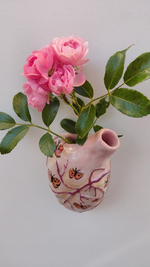 Vase formet som et hjerte med malede sommerfugle, der indeholder en gren med pink roser og grønne blade. (1)