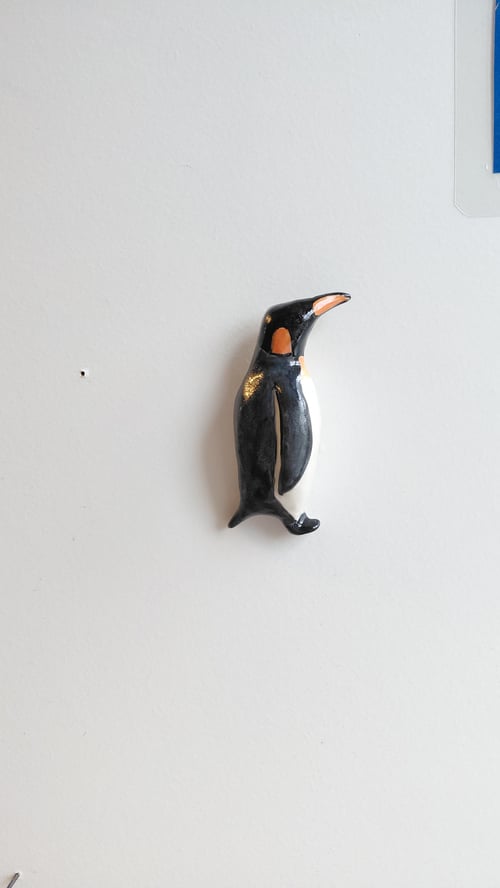 En lille sort, hvid og orange pingvinfigur hængende på en hvid væg. (1)