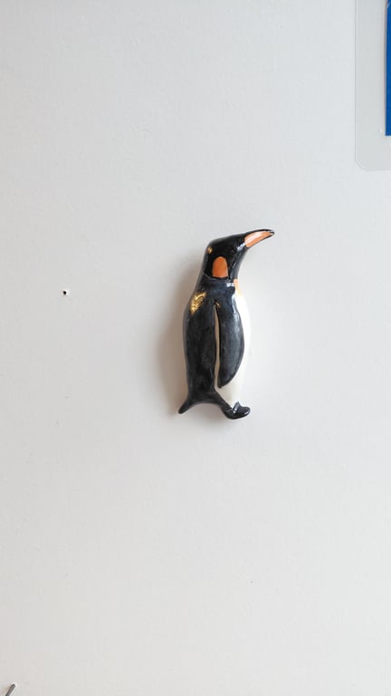 En lille sort, hvid og orange pingvinfigur hængende på en hvid væg.