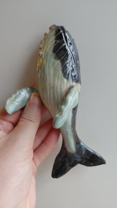 Hånd holder en keramisk figur formet som en hval med finner. (1)