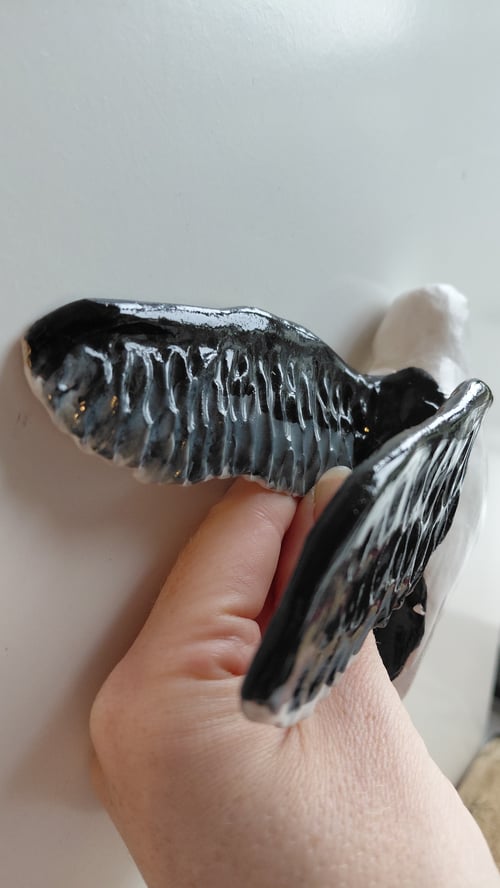 Hånd der holder en sort og hvid keramisk figur formet som en fugl med udstrakte vinger. (3)