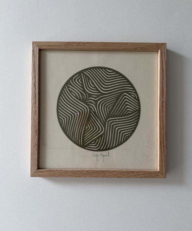 Indrammet kunsttryk med cirkulært mønster bestående af buede, parallelle linjer i sort på beige baggrund.