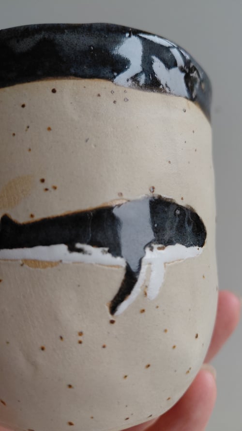 Keramikkrus med sort-hvid hvalmotiv og sort kant, holdt i hånd. (5)