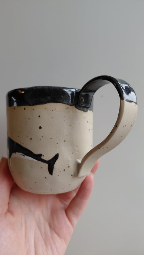 Hånd, der holder en keramikkop med beige glasur og sorte malede detaljer. (8)
