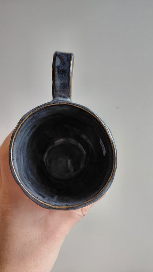 Hånd holder en sort glaseret keramikkop set ovenfra mod en grå baggrund. (10)
