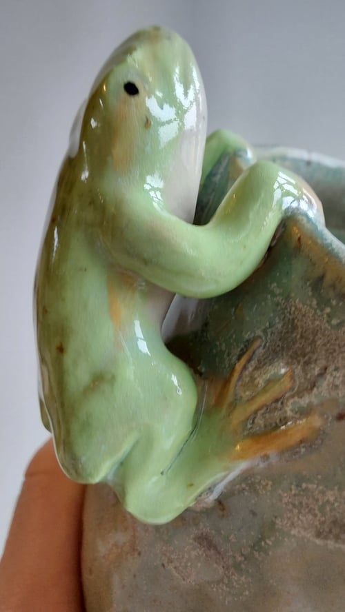 En glaseret keramikfigur af en grøn frø, der klatrer op ad siden af en vase. (5)