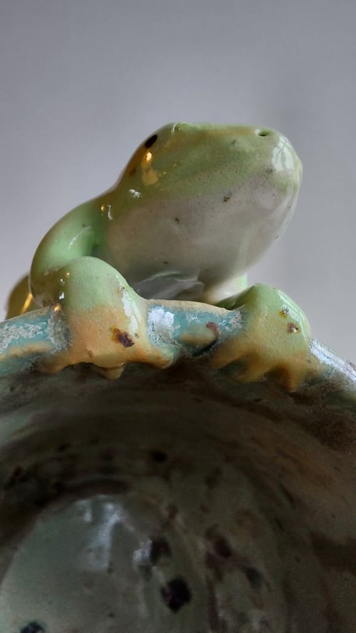 Keramisk figur af en grøn frø siddende på kanten af et krus med glasur. (6)