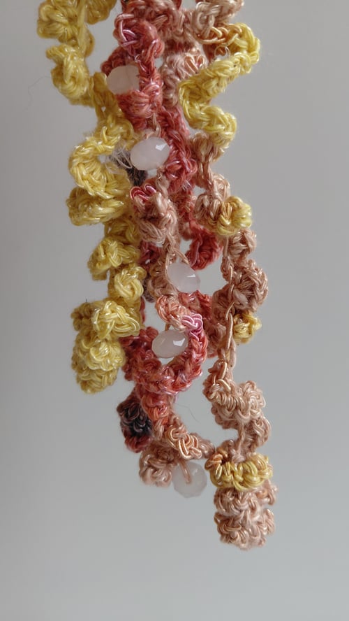 Nærbillede af hæklede blomster i gule, rosa og brune farver med små hvide perler. (4)