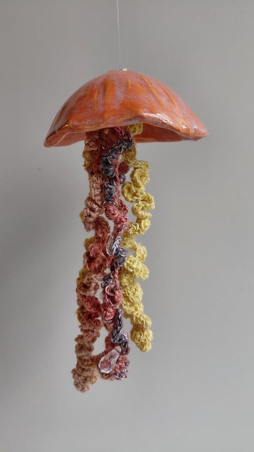 Hængende kunsthåndværk, der forestiller en meduse med orange skærm og farverige, krøllede tråde som tentakler. (5)